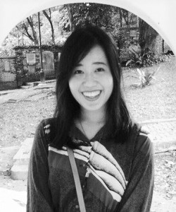 Black and white image of a long-haired female-presenting person in a long-sleeved shirt, smiling into the camera.