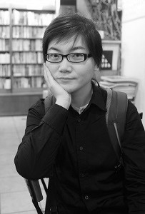 A person in glasses and a long-sleeved collared black shirt. They have their chin resting on their right hand.