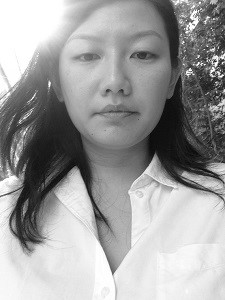 Black and white image of a female-presenting person with long hair wearing a white shirt, looking into the camera.