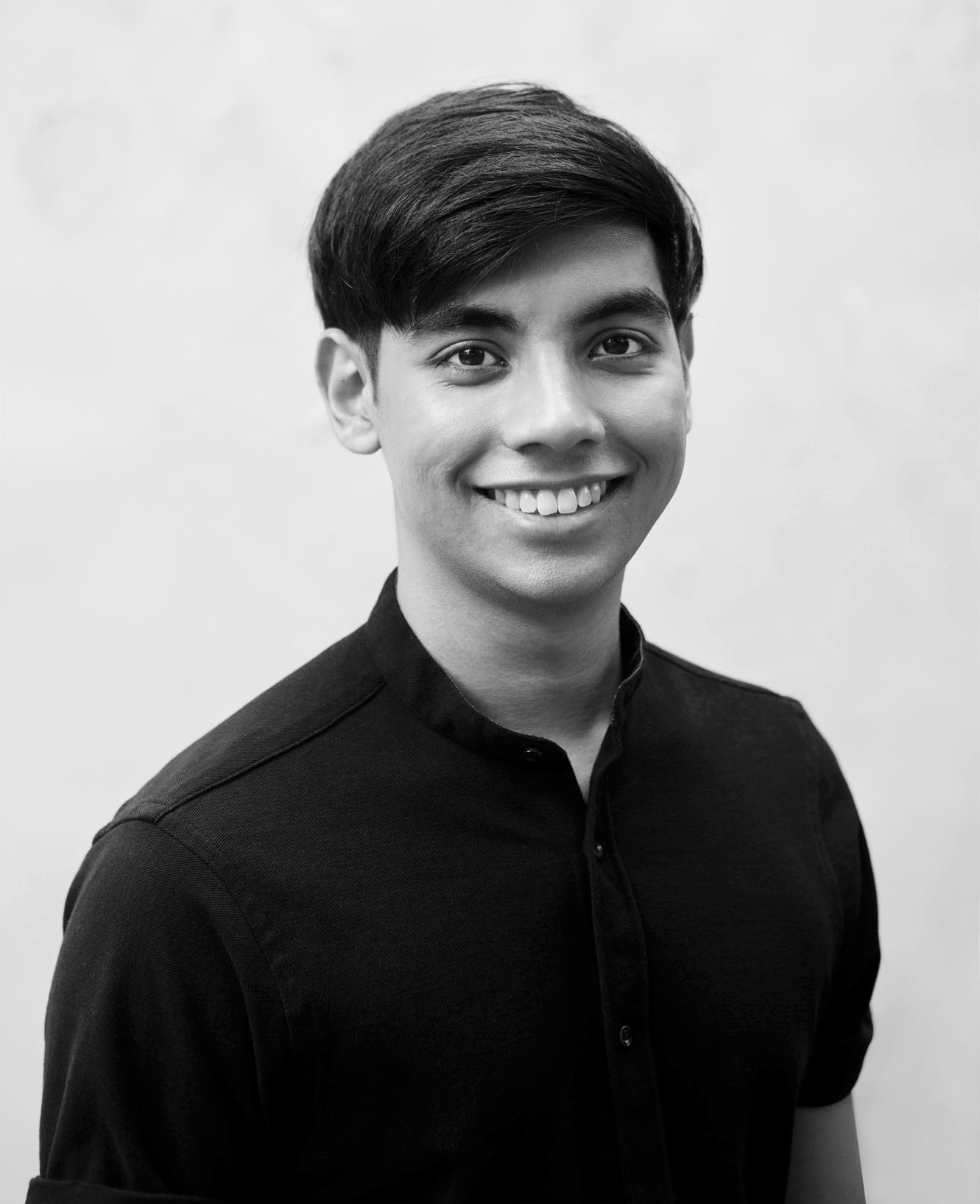 Black and white image of a male-presenting person in a black shirt, smiling into the camera.