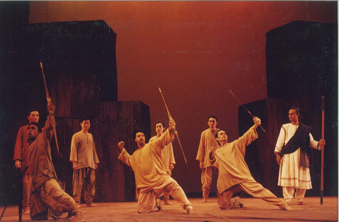 Three persons kneeling and miming pulling back bows, observed by five other persons standing around them.