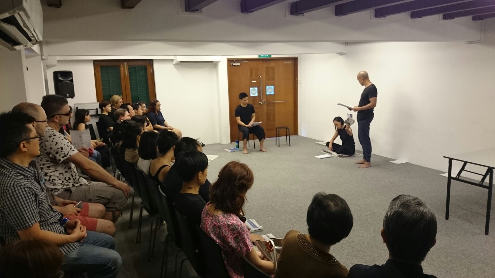 Three figures appear to be reading their scripts in a room, separated by audiences seated at the back.