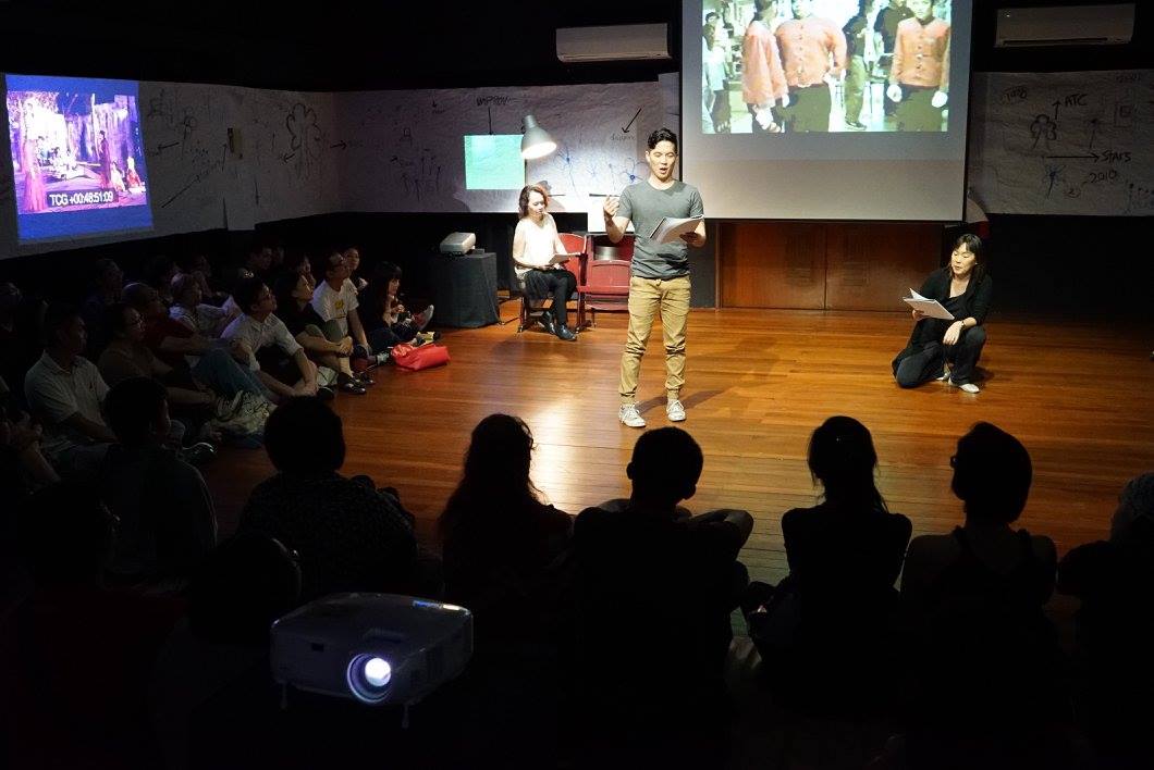 The actors on stage, Shou Chen standing centrestage, Nora seated to the back and Serene squatted to the right. An audience looks on.