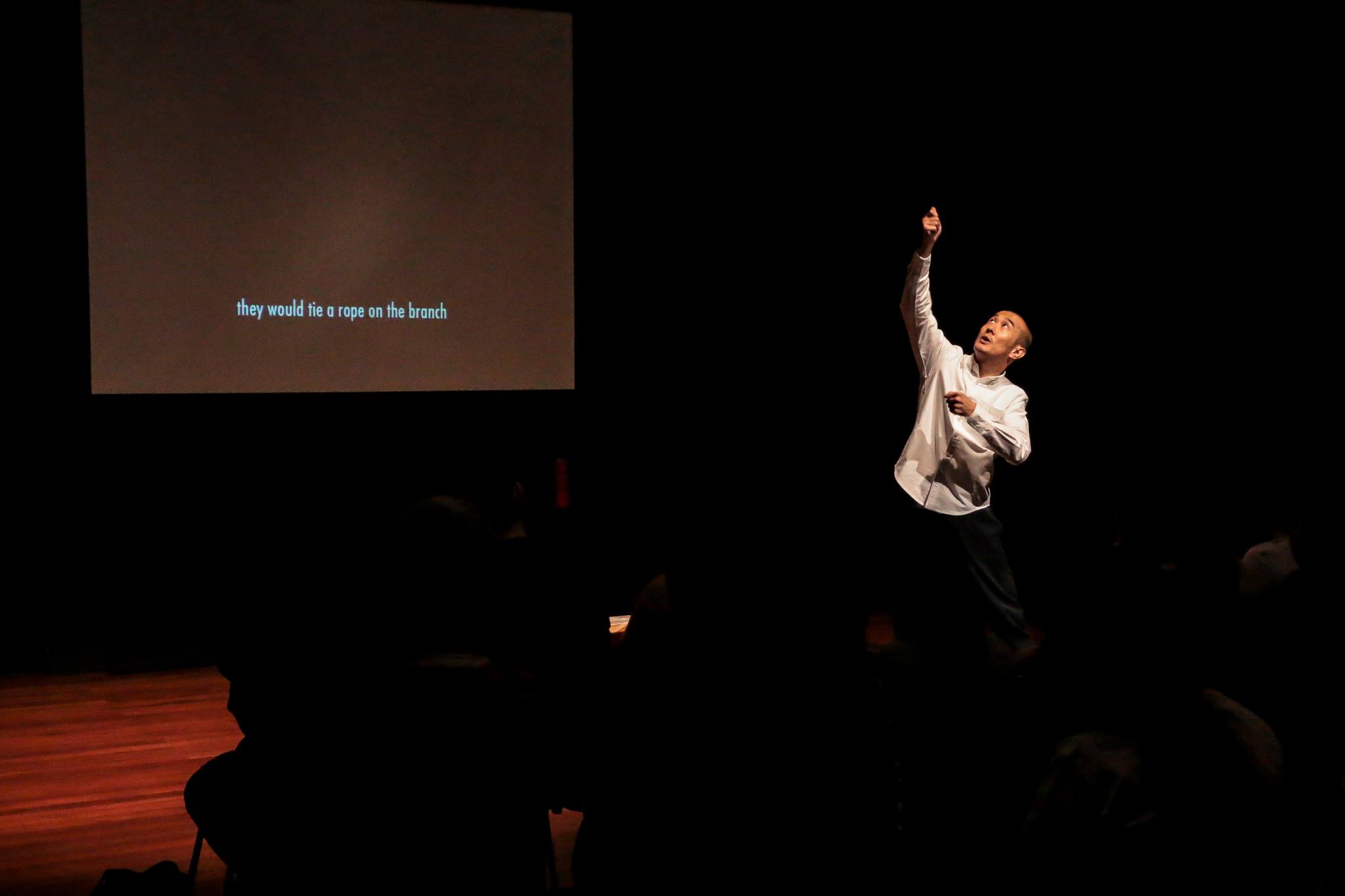 The photograph features a man looking up and mimicking the action of holding on to a rope. A screen behind him reads "they would tie a rope on the branch".