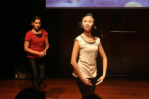 Two female-presenting persons, the one in the foreground in a sleeveless white top and the one in the background in a short-sleeved red shirt, dancing in the 42 Waterloo Street Black Box.