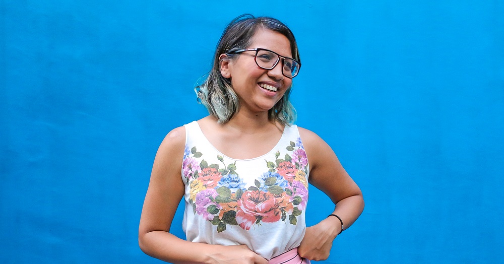 Nabilah Said standing in front of a blue wall, looking to the left and smiling.