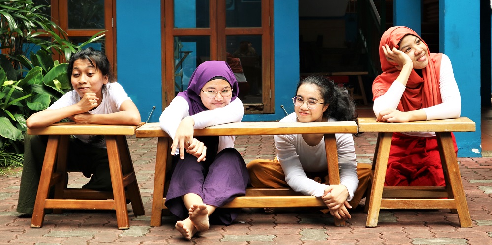 Four female-presenting persons sitting and kneeling along some wooden benches in the rear courtyard of 42 Waterloo Street.