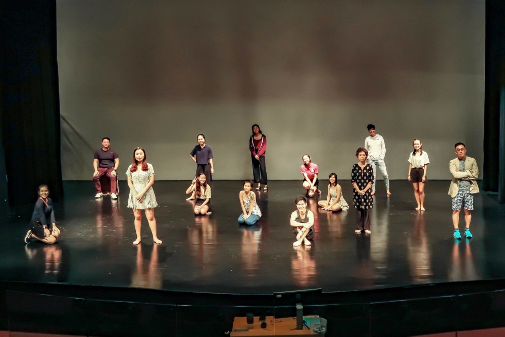 A large group of people standing, sitting and kneeling on a stage, smiling into the camera.