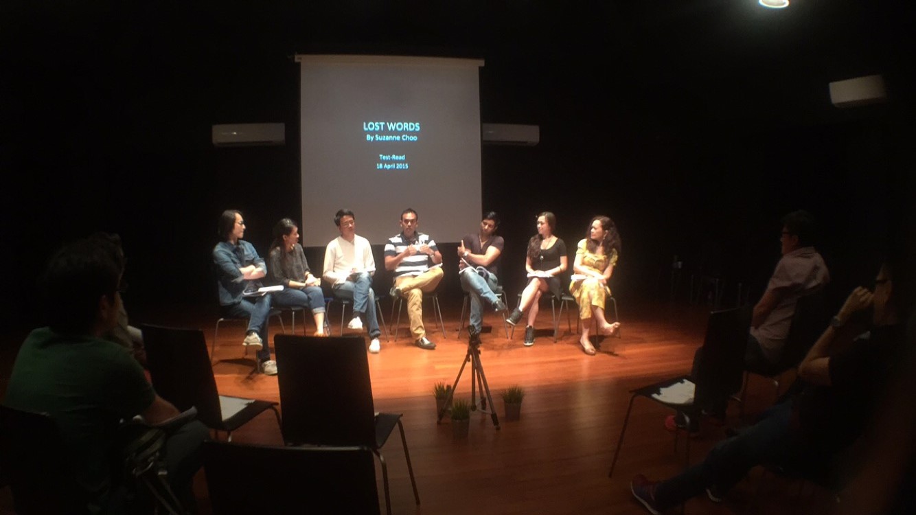 Seven persons seated in a row in a black box. Behind them is a screen with the words 'LOST WORDS by Suzanne Choo' projected on it.