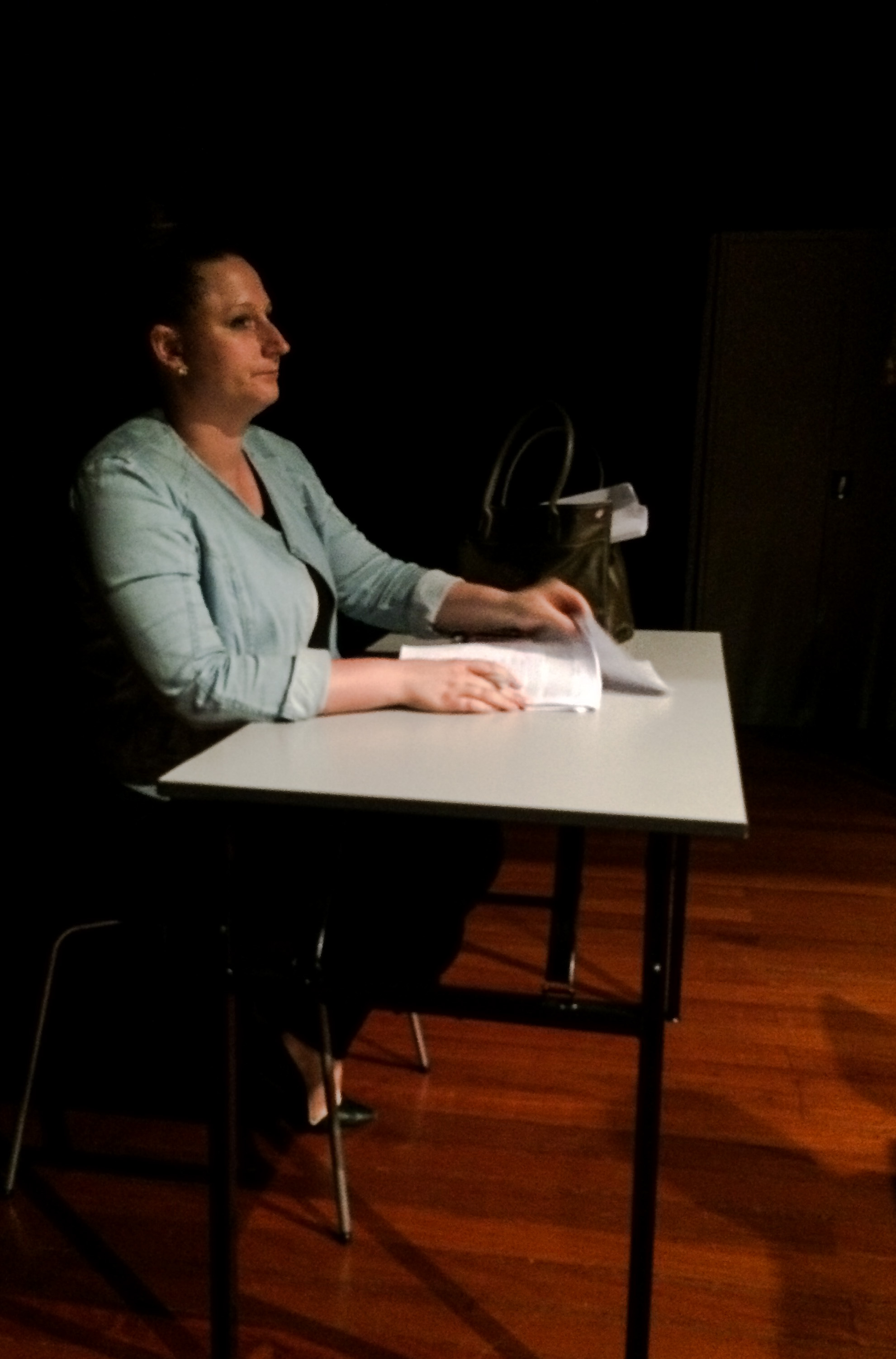 A female-presenting person in a long-sleeved light blue top seated at a table with a script in front of her.