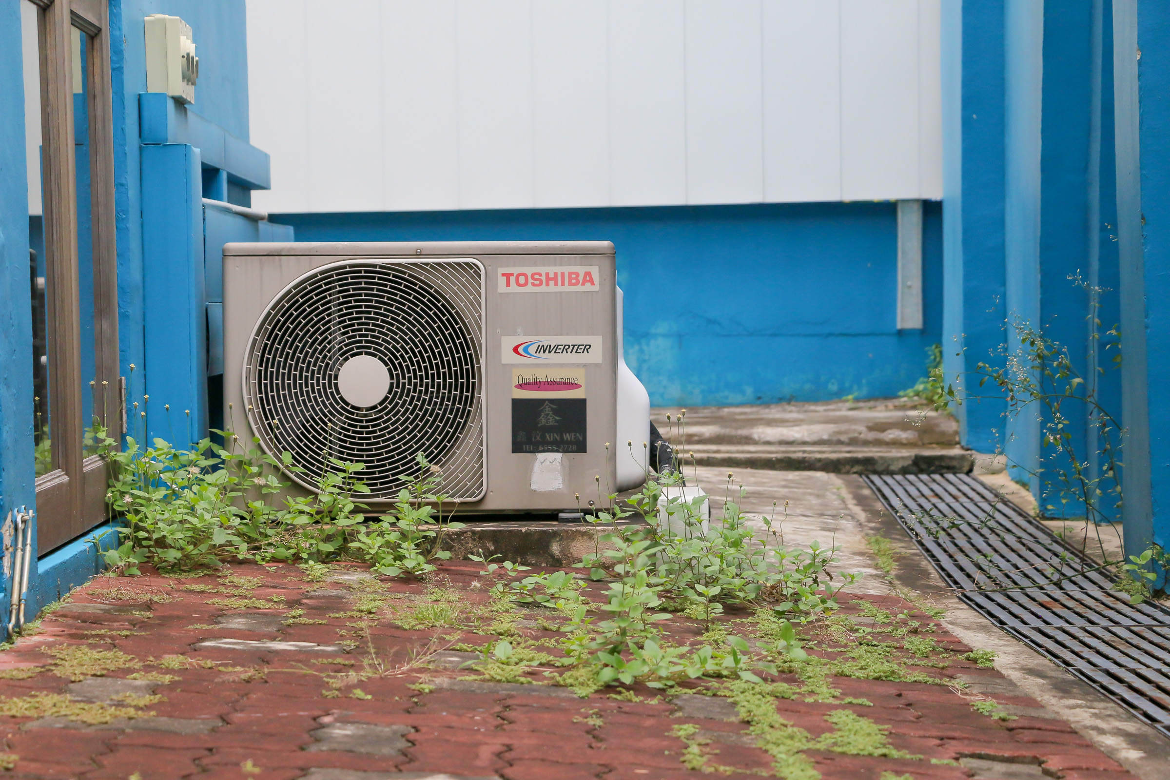 An inverter on the tiled brick ground. Weeds grow in the cracks on the ground around it.