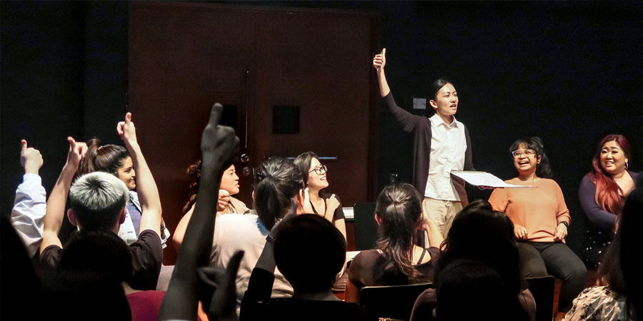 A group of people with their hands raised in a thumbs-up in the 42 Waterloo Street Black Box.