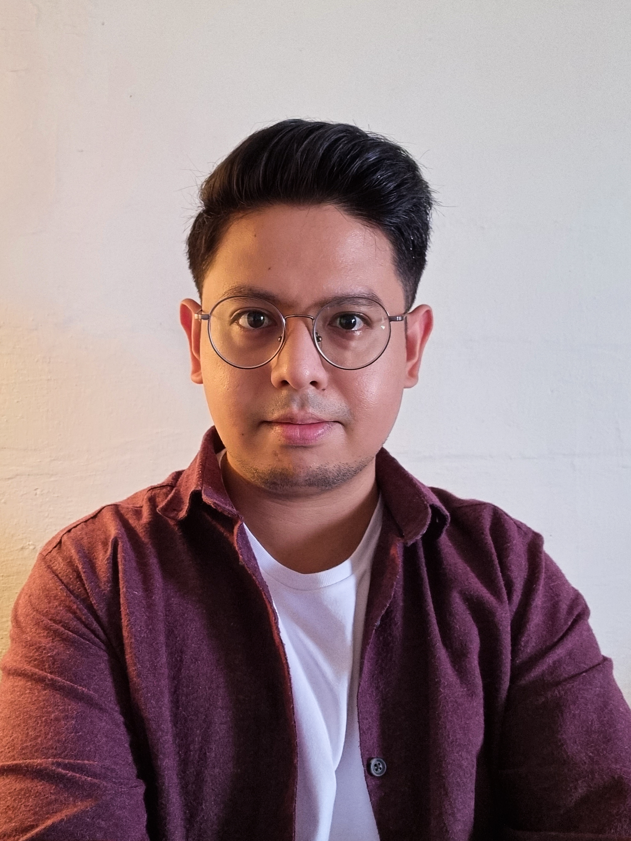 Coloured headshot of a bespectacled Adeeb Fazah, in a white shirt and a maroon outerwear.