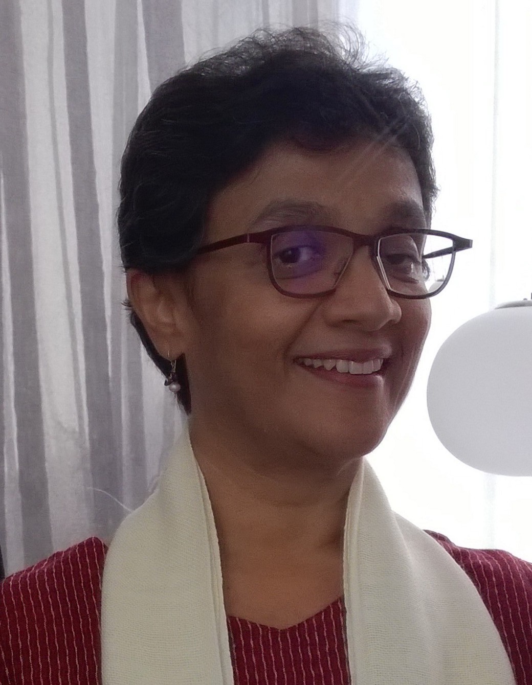 A headshot of Charlene Rajendran wearing a white scarf and glasses, smiling into the camera.