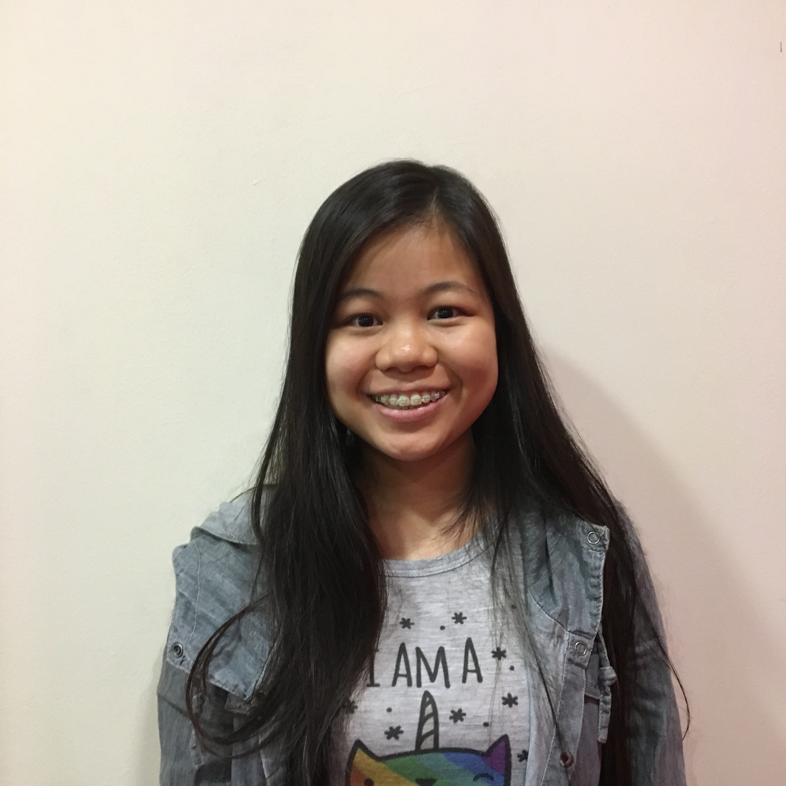 A headshot of Chia Xin Ying in a grey jacket, against a white wall, smiling into the camera.