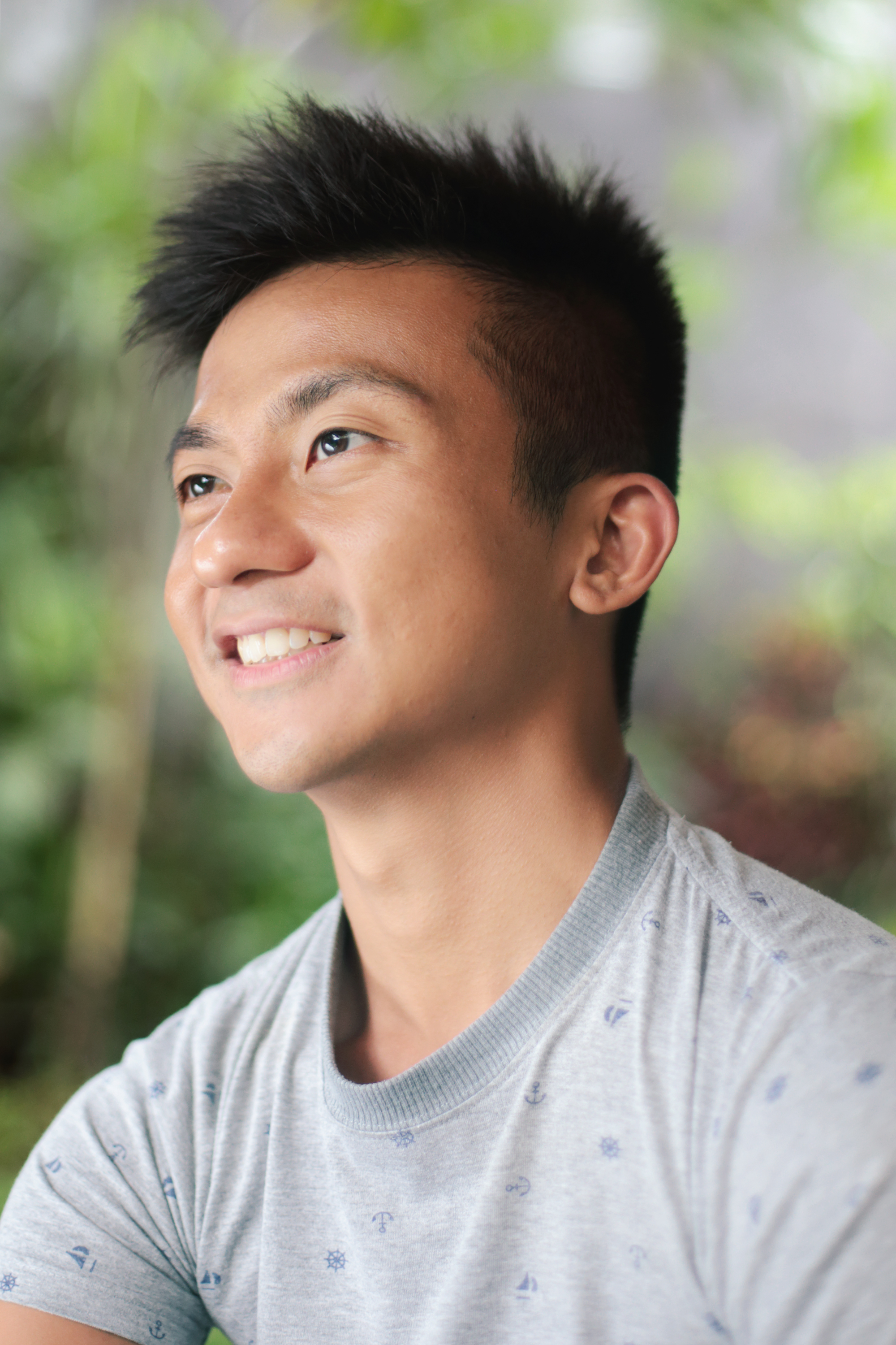 A headshot of Loo Zihan in a grey shirt, facing left, smiling.