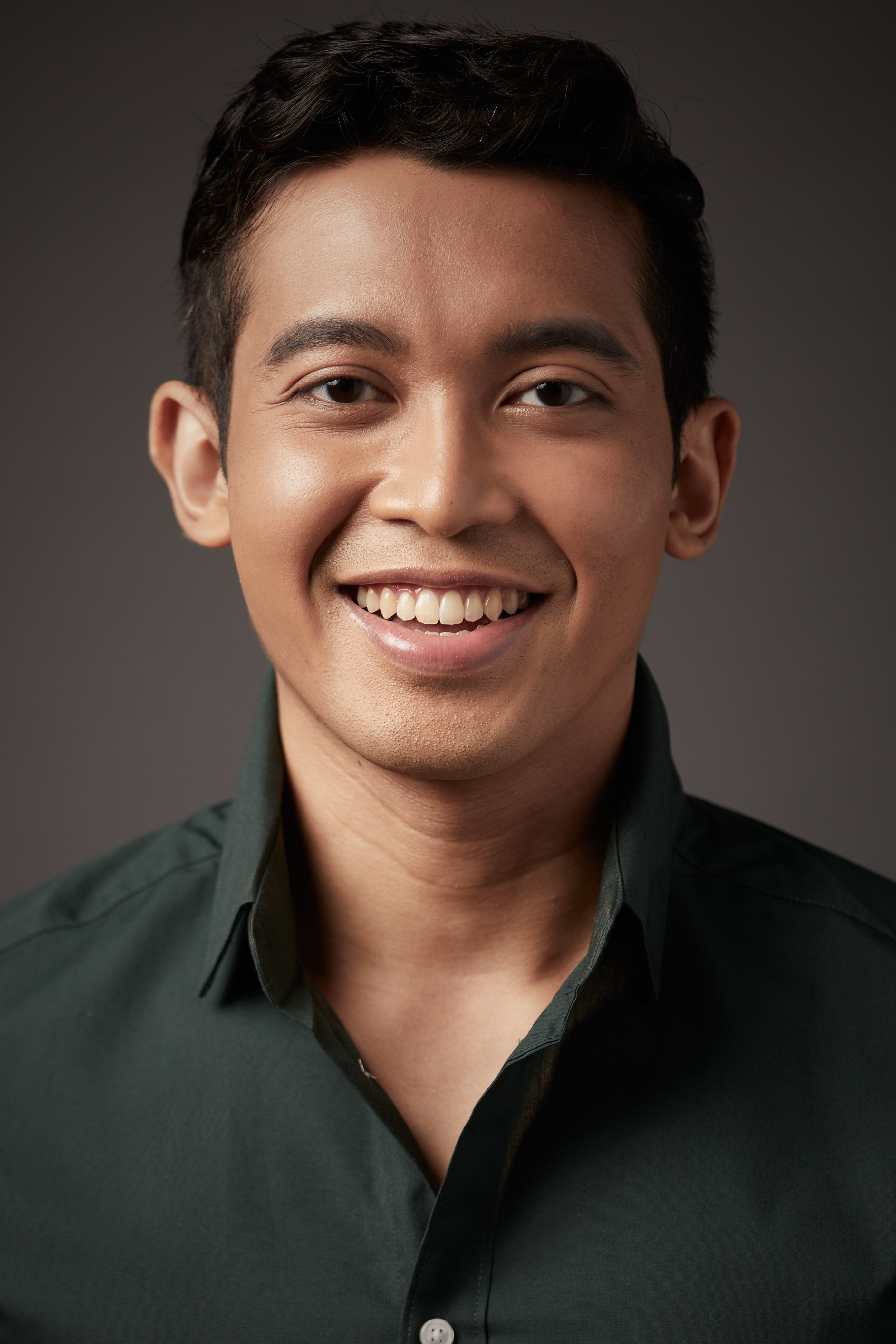 An image of Fadhil Daud smiling, dressed in a black button up shirt.