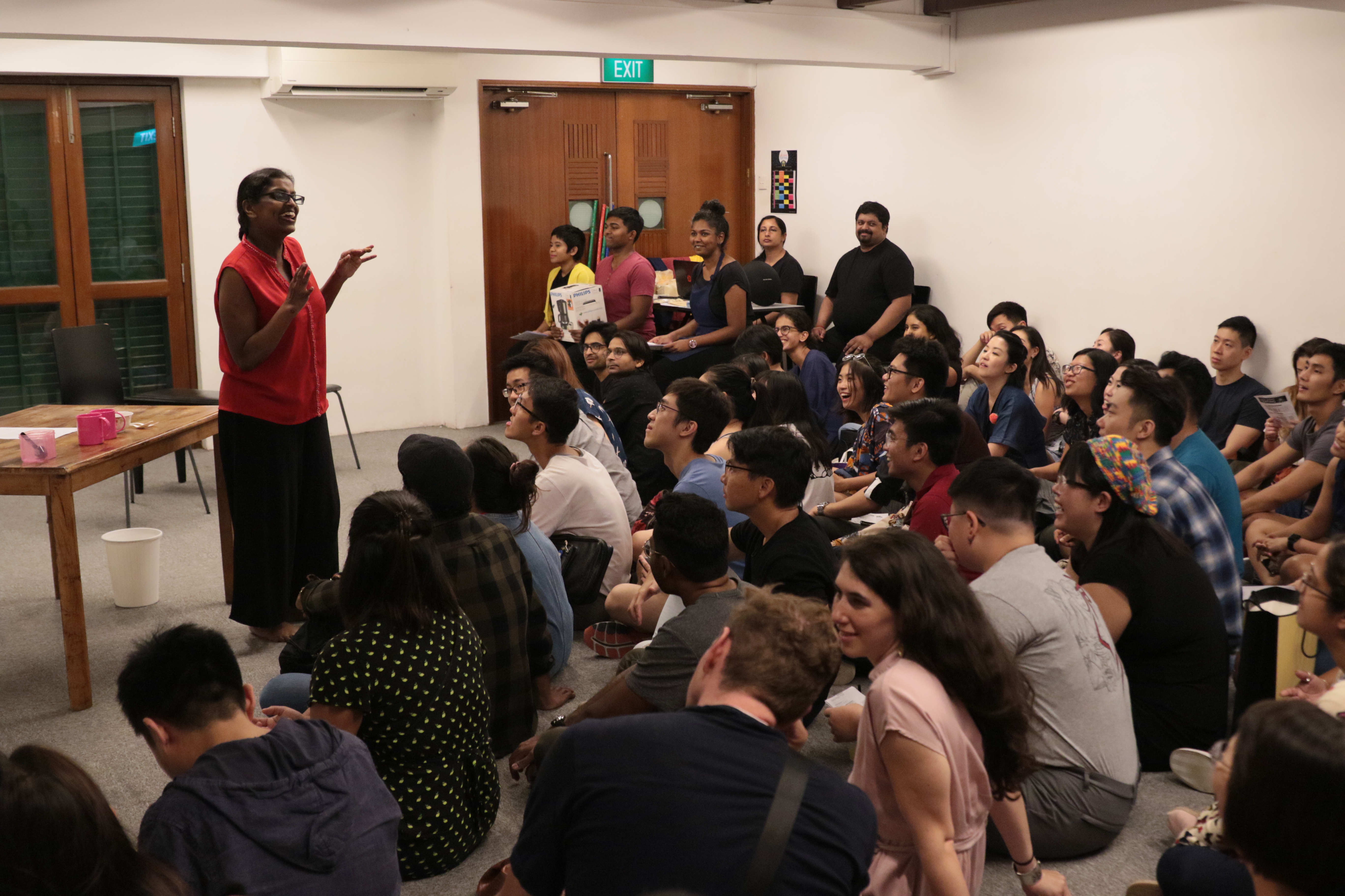 The photograph features a packed room of audience listening to a presenter.