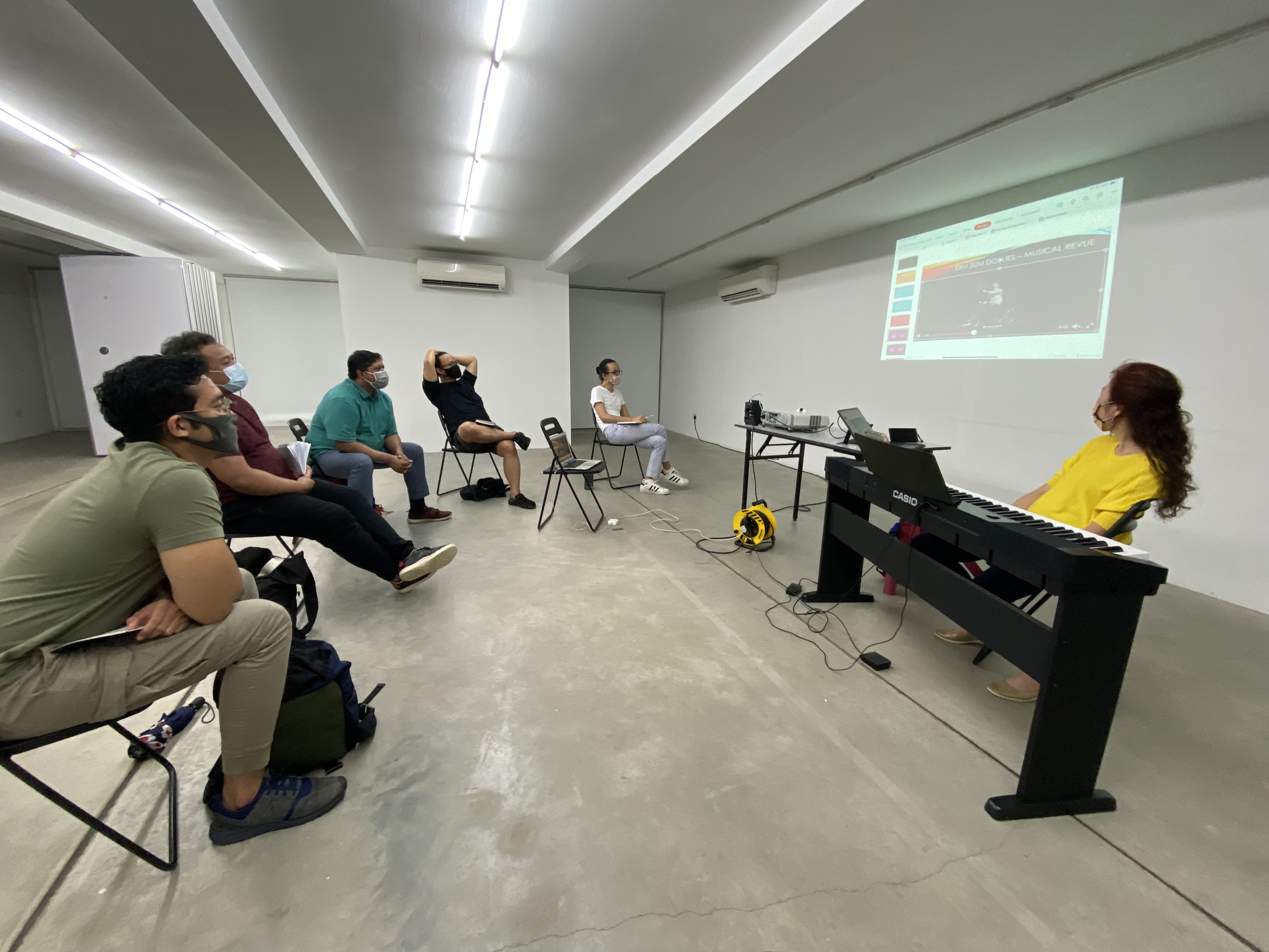 The photograph features a group of people seated and directing their attention to a projected screen.