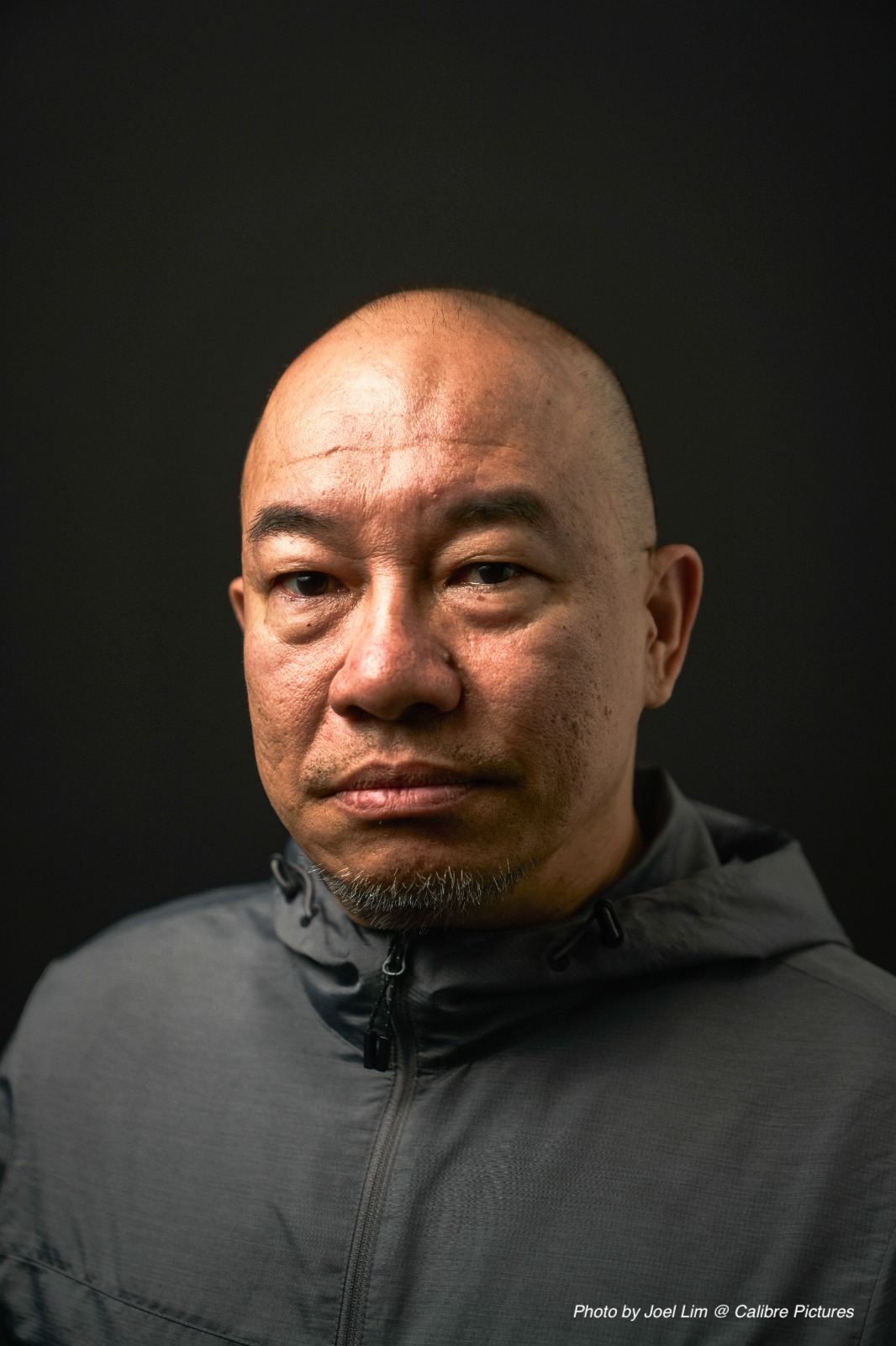 An image of Julius Foo, a bald Chinese man dressed in a grey outerwear.