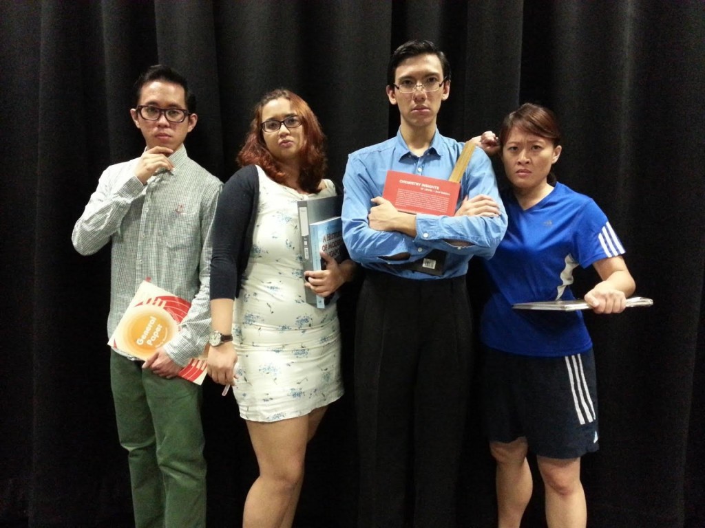 Four persons dressed like teachers, standing in front of a black curtain.