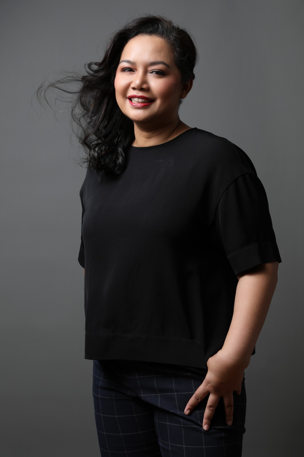 An image of Joanne with curly hair brushed to one side, dressed in an all-black outfit.