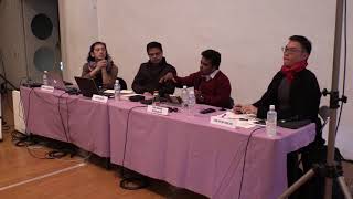 Four persons seated at a pink table in front of a projector screen.