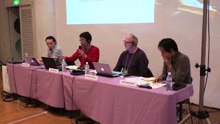 Four persons seated at a pink table in front of a projector screen.