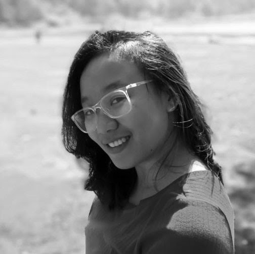 Black and white headshot of Nia Augustina, smiling and wearing glasses.