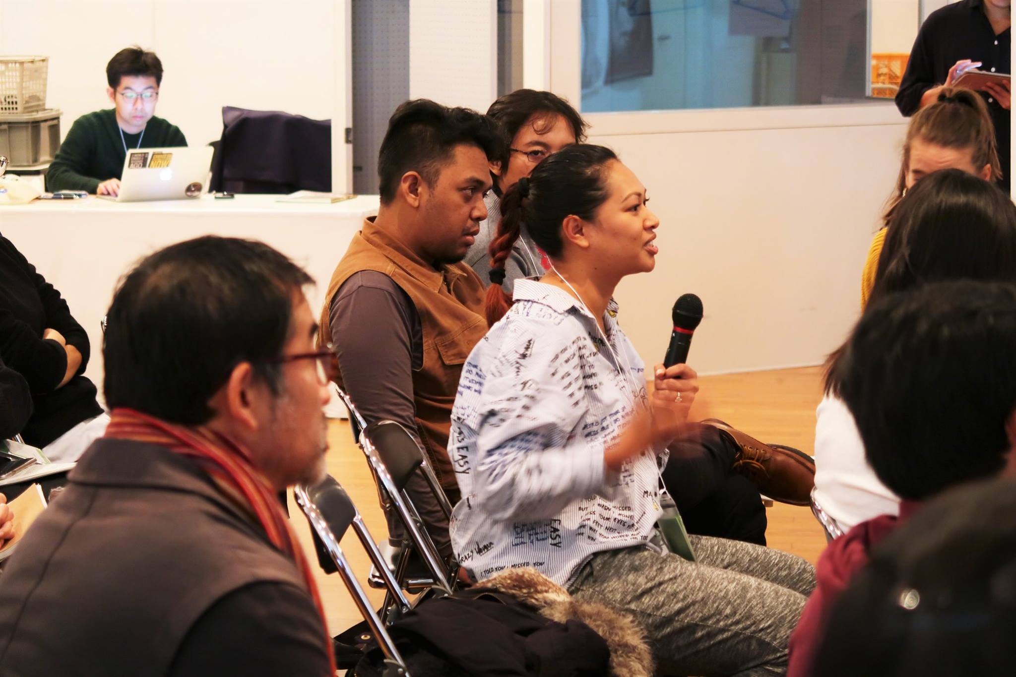 A female-presenting person amidst a large audience, speaking into a microphone.