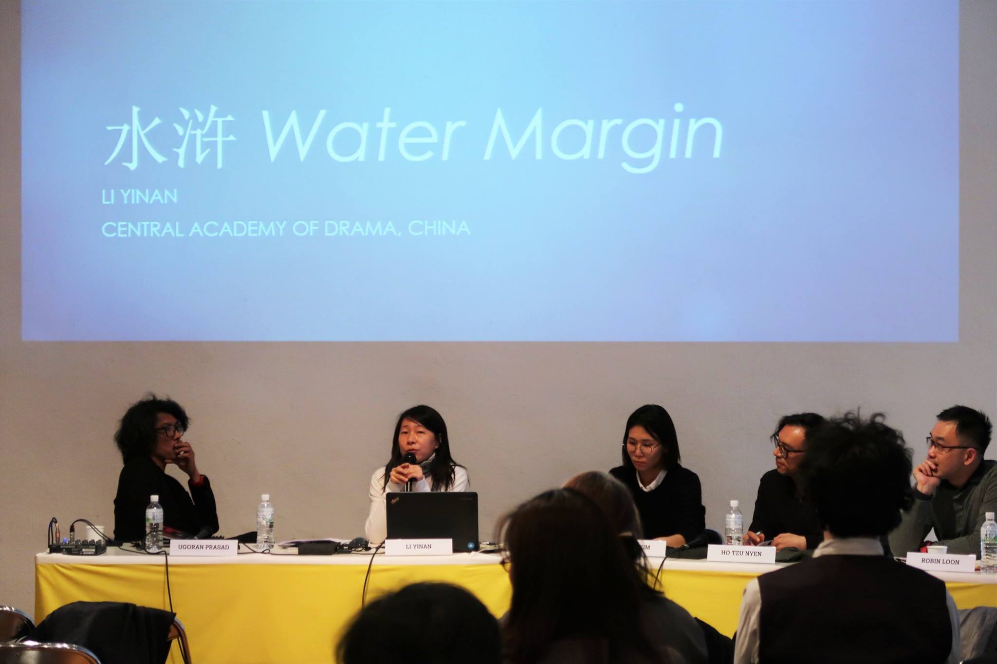 Five persons seated at a long table. Above them is a projector screen featuring a blue side with the words 'Water Margin'.