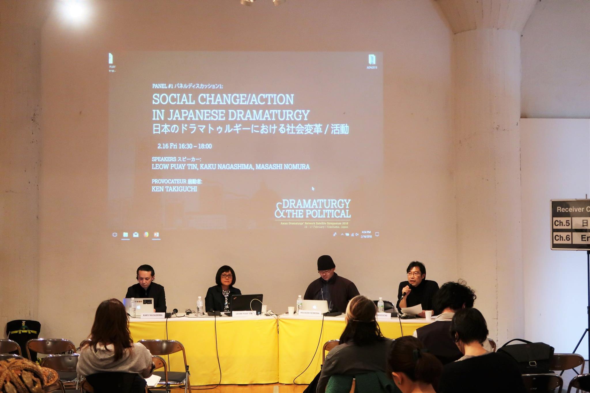 Four persons seated at a long table. Above them is a projector screen.