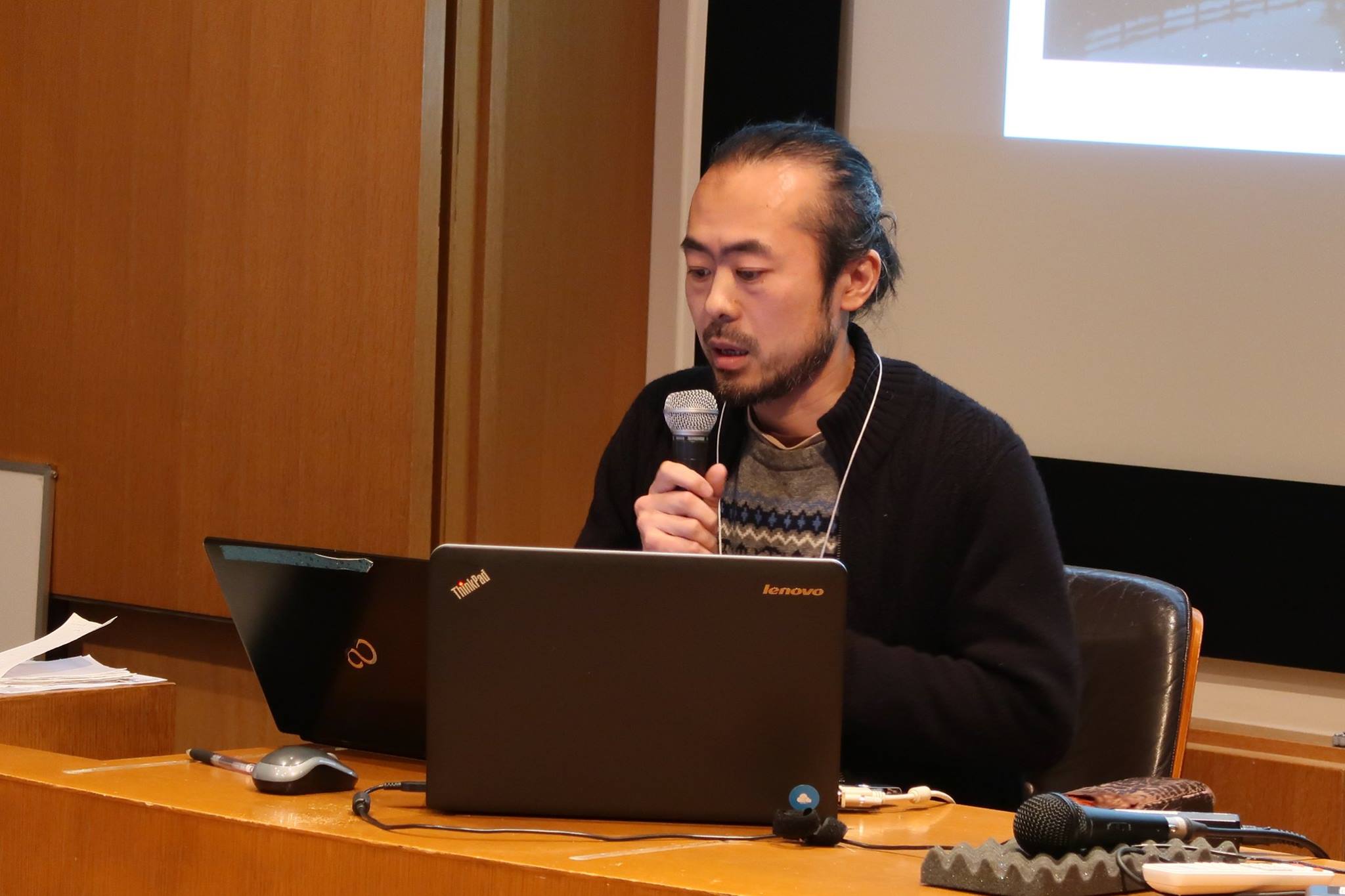 A male-presenting person looking at his laptop, speaking into a microphone.