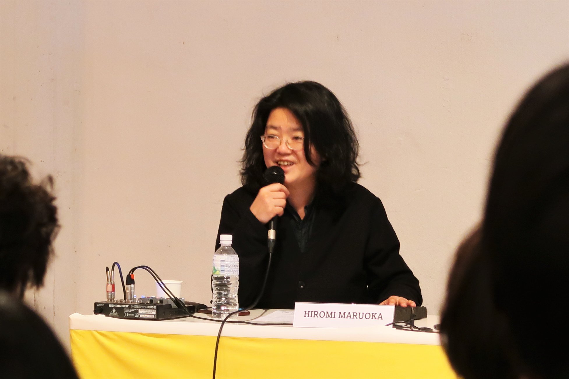 A female-presenting person smiling as she speaks into a microphone.