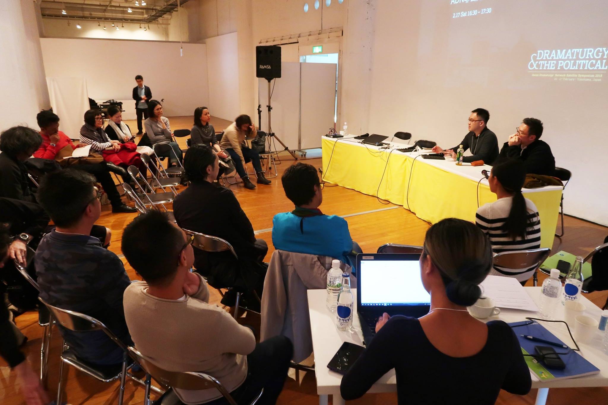 A semicircle of audience members facing a long table, at which two persons are seated.