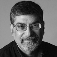 Black and white headshot of Rustom Bharucha, with a beard and glasses.