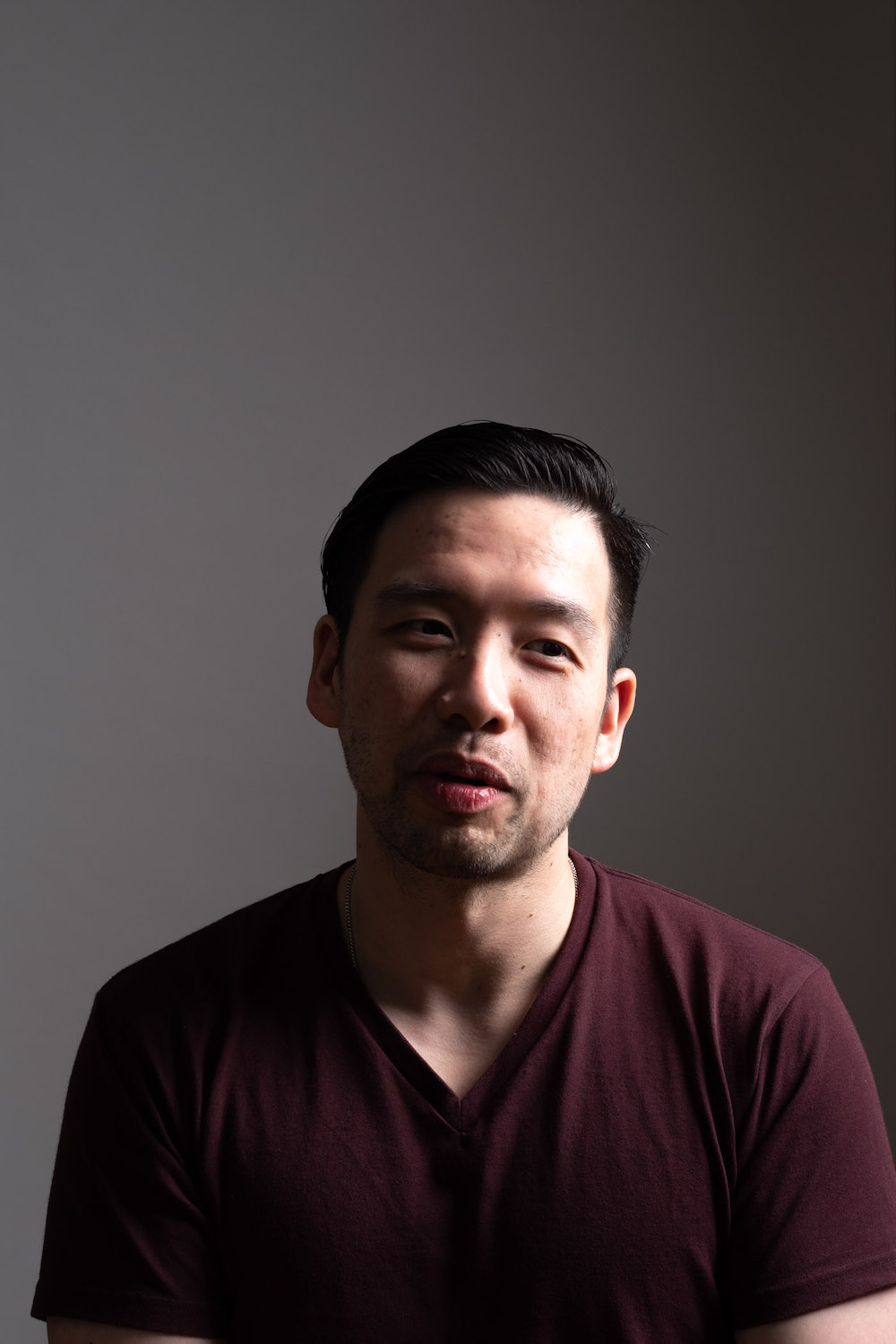 Headshot of Ivan Choong, glancing away from the camera, wearing a dark red shirt.