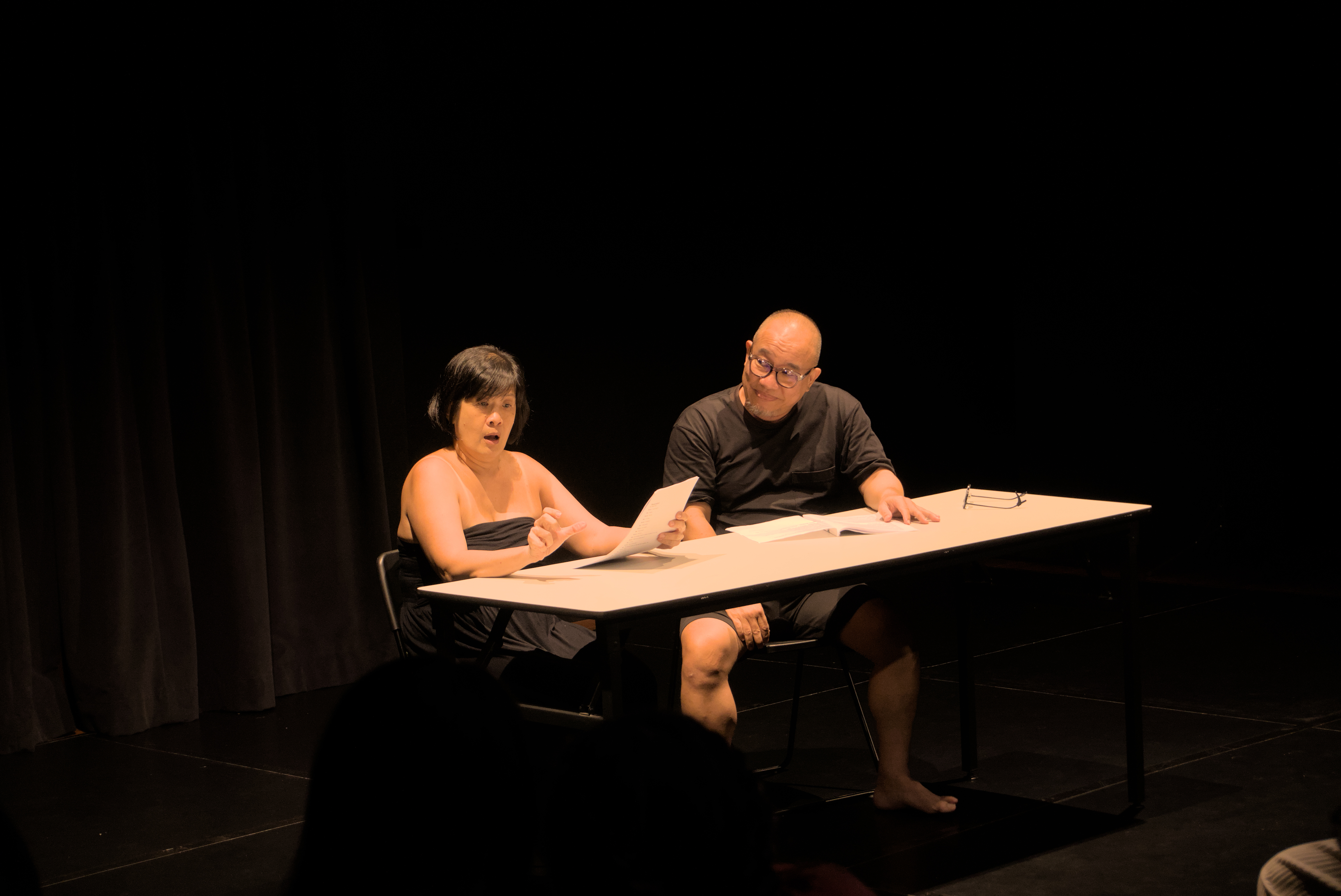 Karen Tan and Julius Foo are seated at a table, Karen having a shocked expression on her face as Julius looks on.