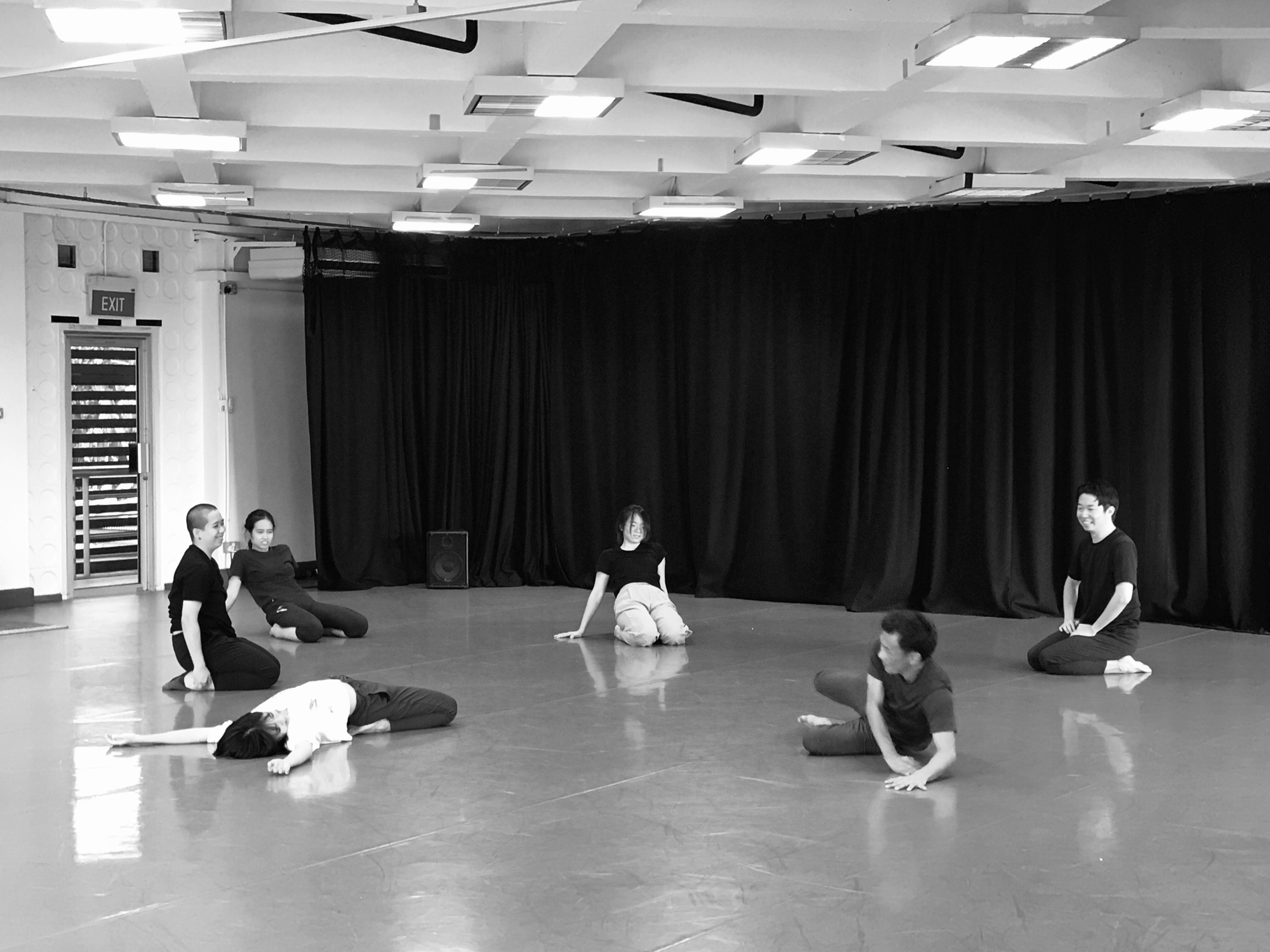 A black and white photo of the members of ZOBO Company seated and sprawled across the studio in discussion.