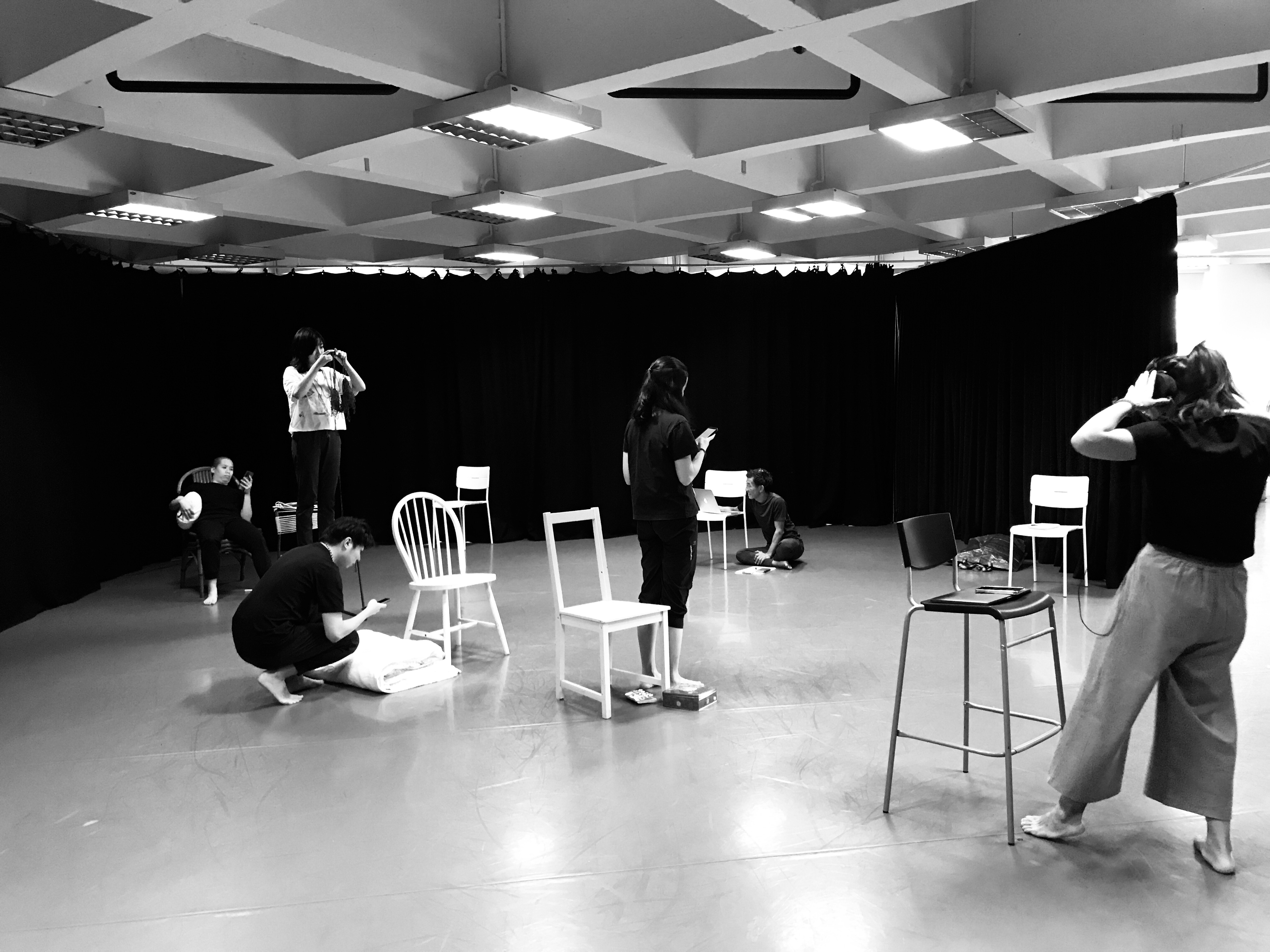 A black and white photo of the members of ZOBO Company in various seating and standing positions spaced out in the studio.