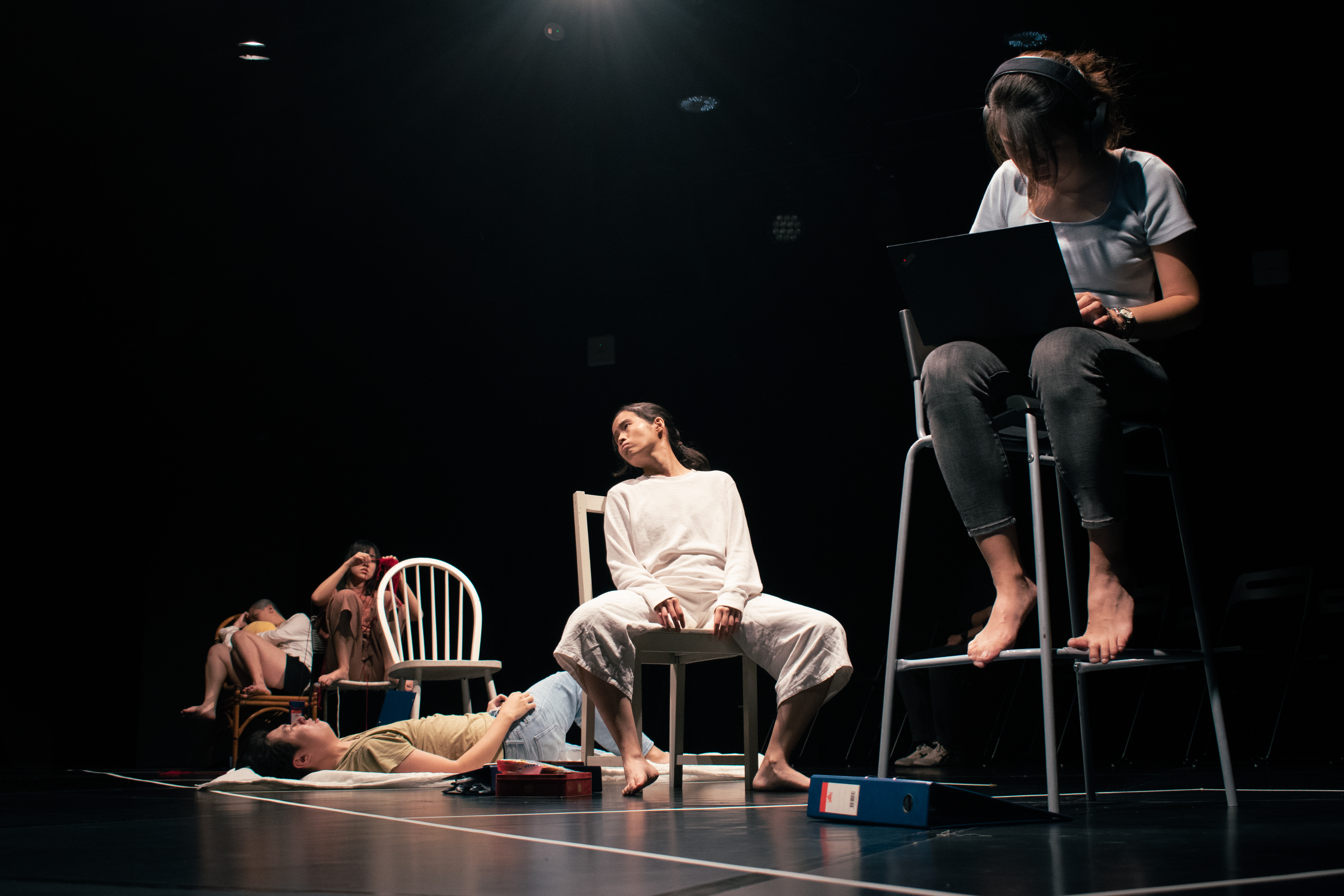 An image of members of ZOBO Company in the Black Box some seated on different chairs, one laying on the floor.