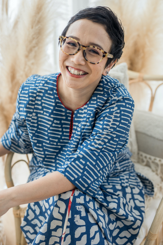 Oniatta Effendi in a blue outfit and glasses, seated and smiling.