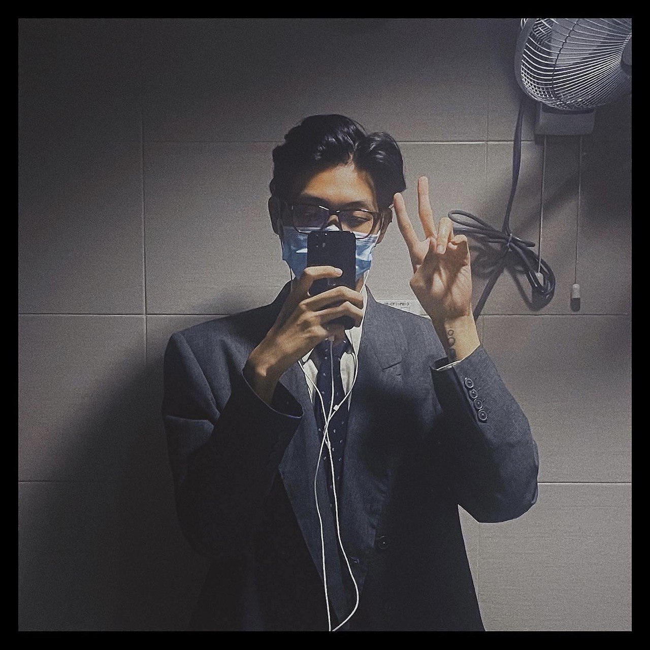 Half-body selfie of Wisely Chow, wearing a mask, suit and tie, doing a peace sign.