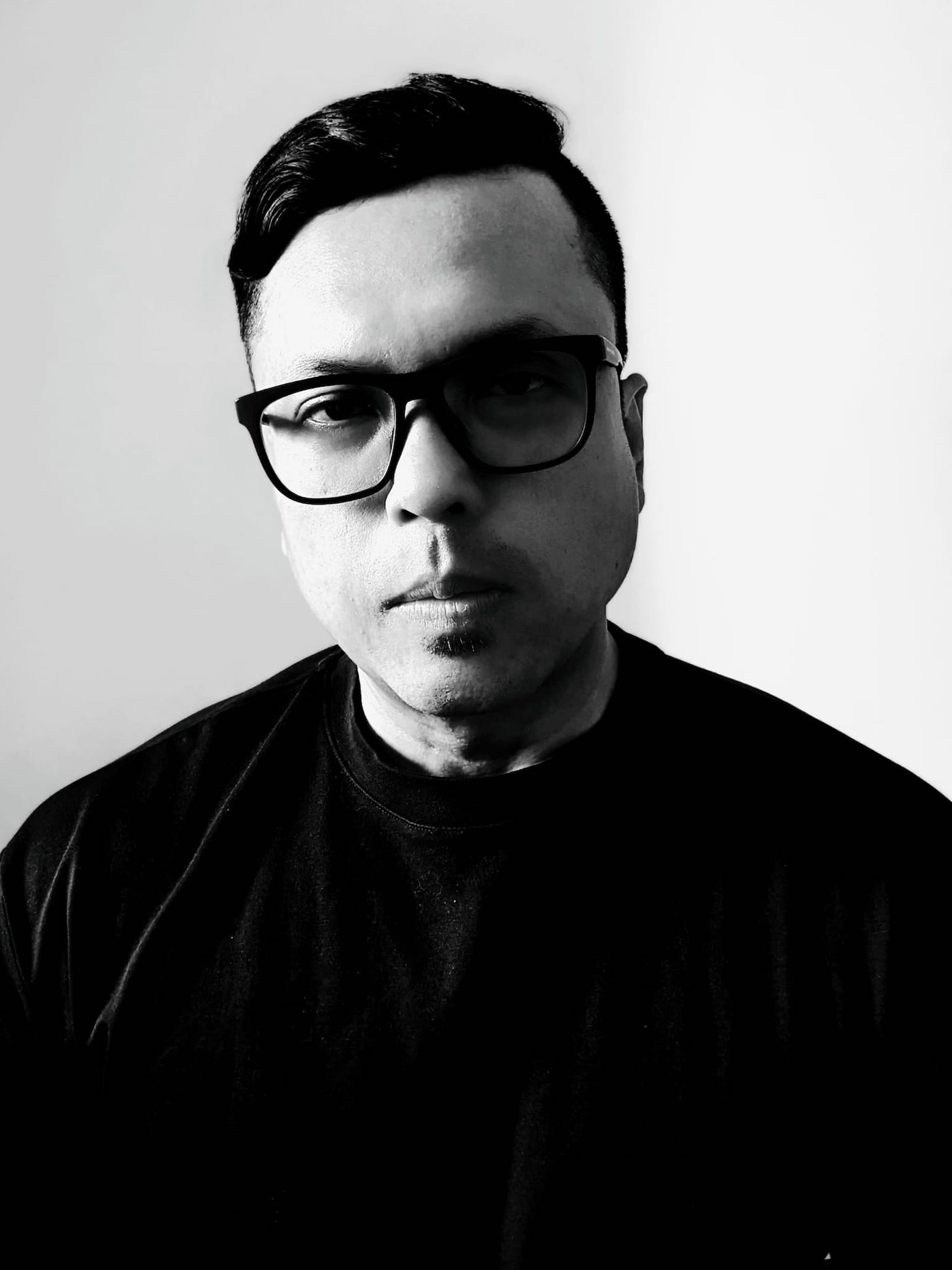 Black and white half-body shot of Zulfadli Rashid in glasses and a black shirt, with a neutral expression.