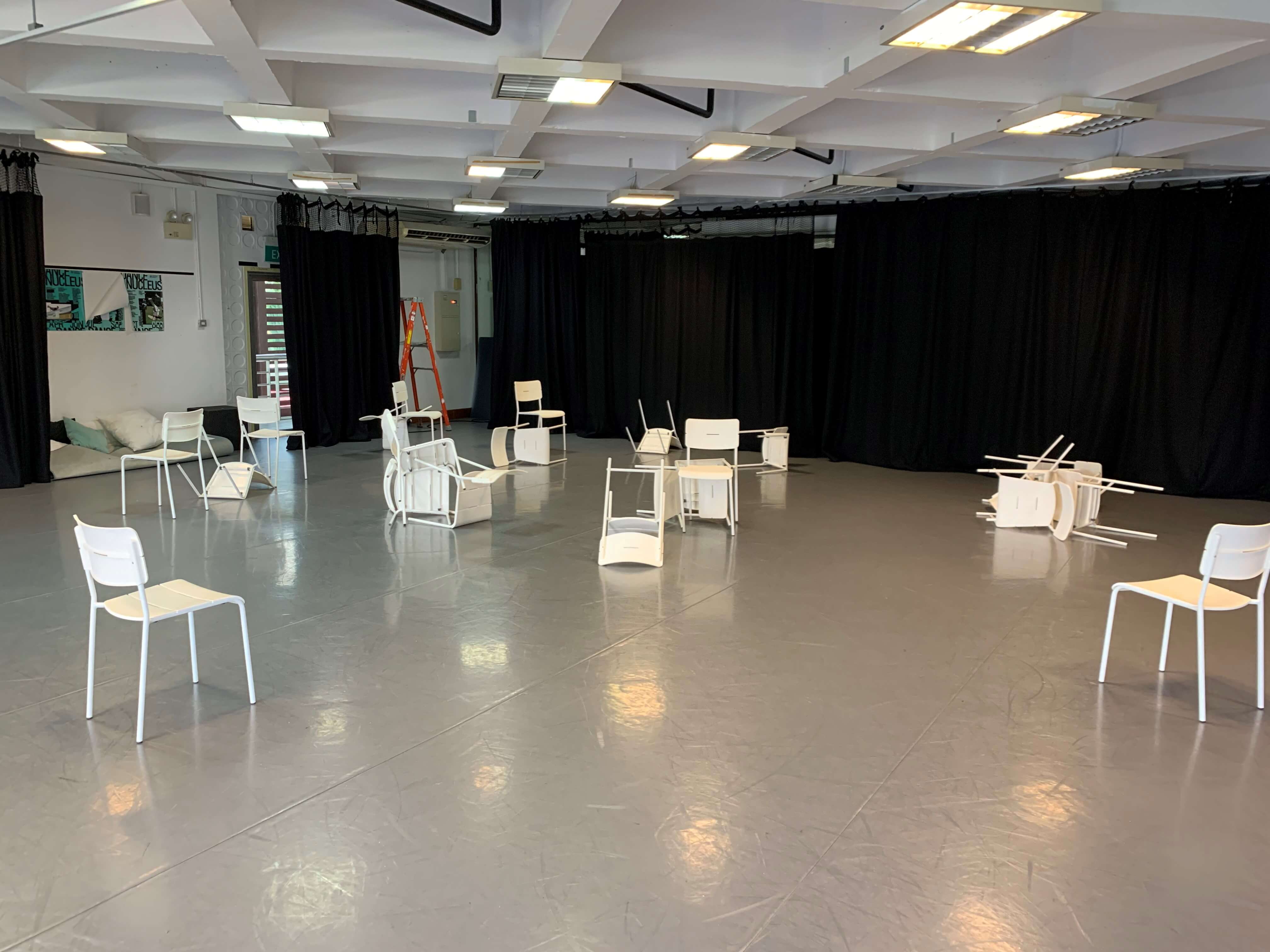 The photograph features a room with a number of white chairs in varoius orientations spread out across the room.