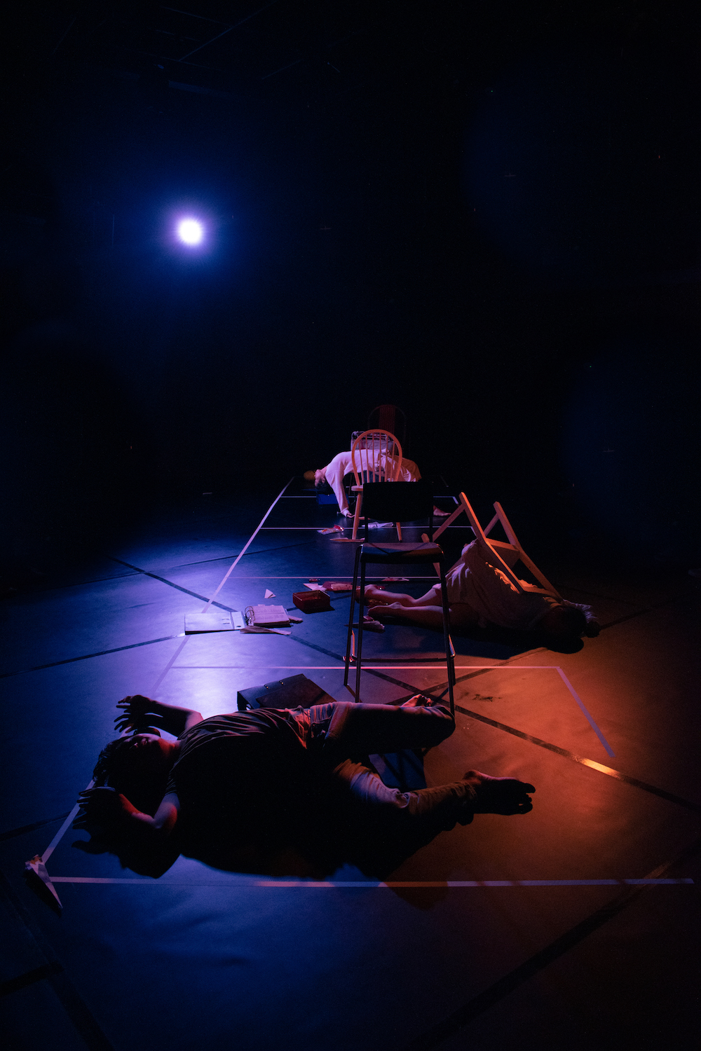 An image of ZOBO Company in a dimly lit Black Box, silhouettes of them laid across the floor and chairs.