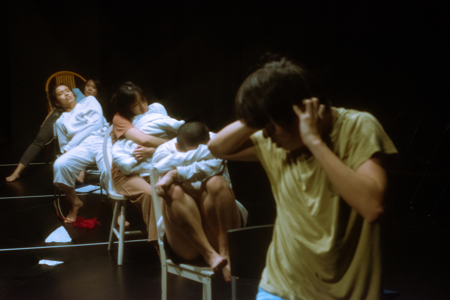 An image of ZOBO Company members in the Black Box, four seated in chairs in various positions, one standing in front with hands on their ears, head turned to the back.