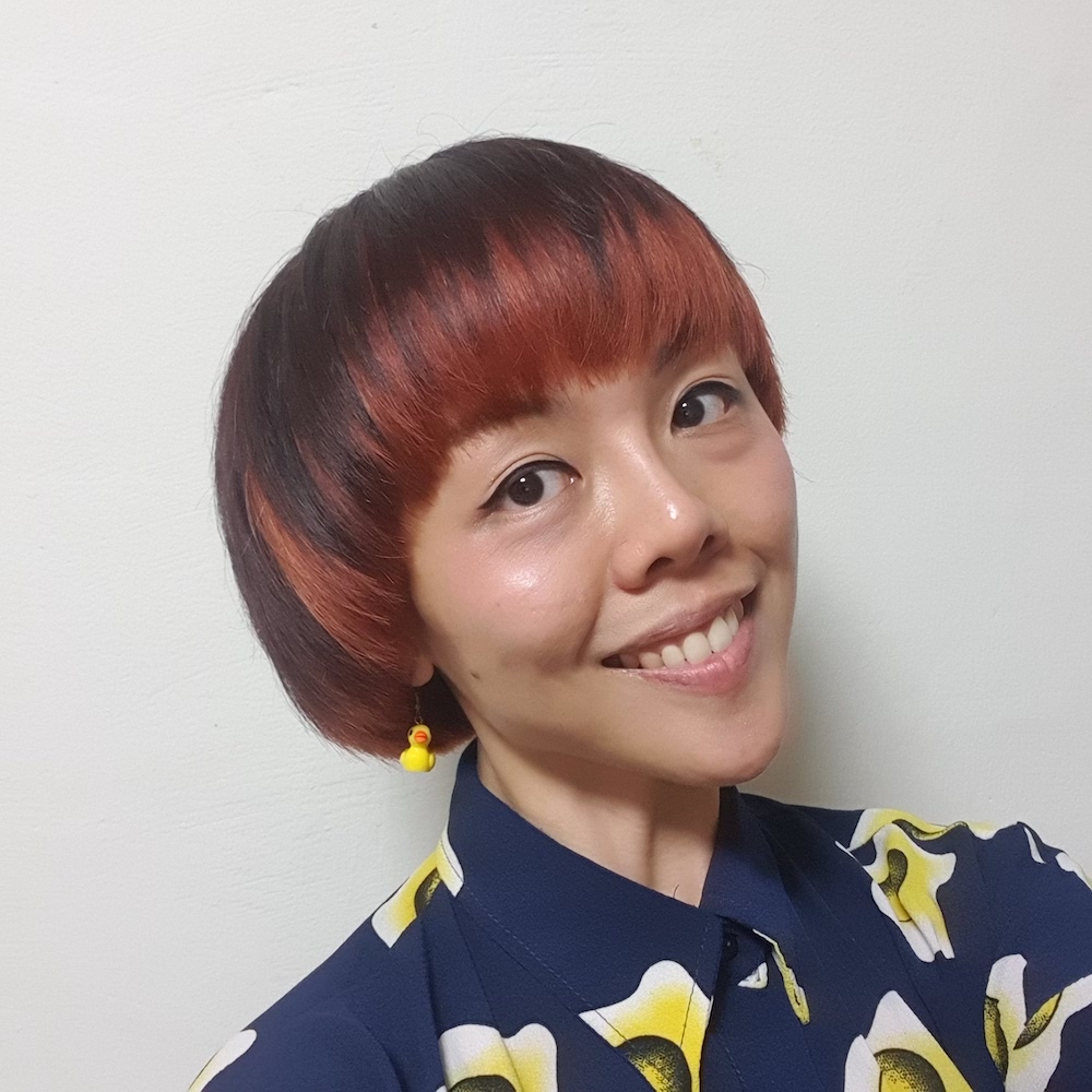 Headshot of Audrey Luo wearing earrings and a blue collared shirt, head tilted and smiling.