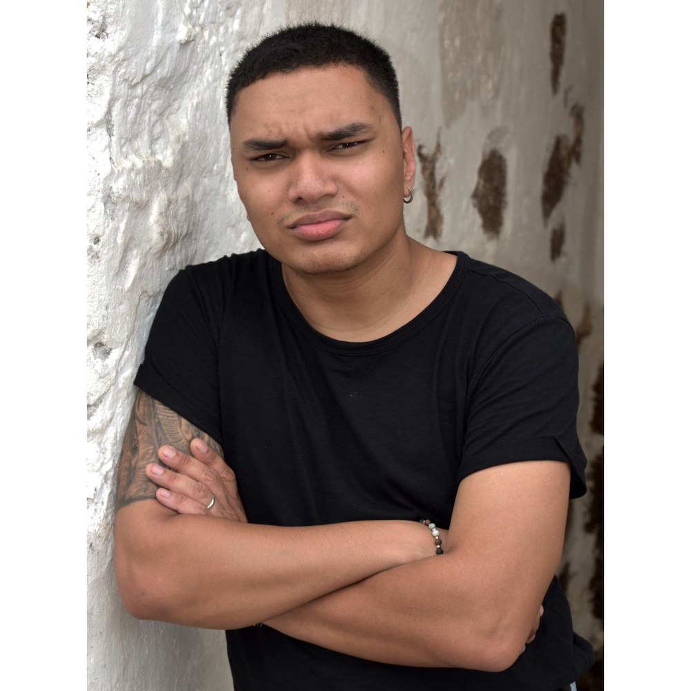 Half-body shot of Joshua Elias in a black shirt, frowning slightly, arms folded.