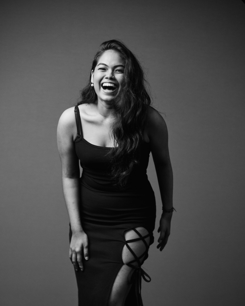 Black and white full-body shot of Periyachi Roshini in a sleeveless black dress, laughing happily.